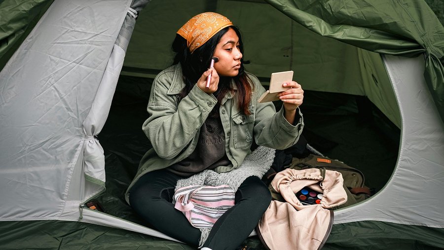 Donna seduta in una tenda mentre si applica il make-up 