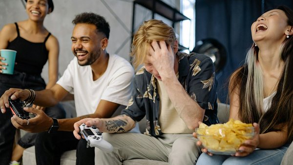 Consigli per convivere in armonia Quattro giovani seduti sul divano ridono mentre giocano a un videogioco