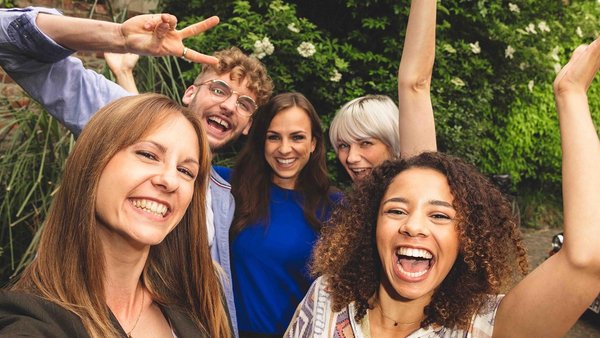 Pianificare una vacanza con gli amici: come funziona Cinque amici in piedi vicini tra loro che ridono davanti all’obbiettivo