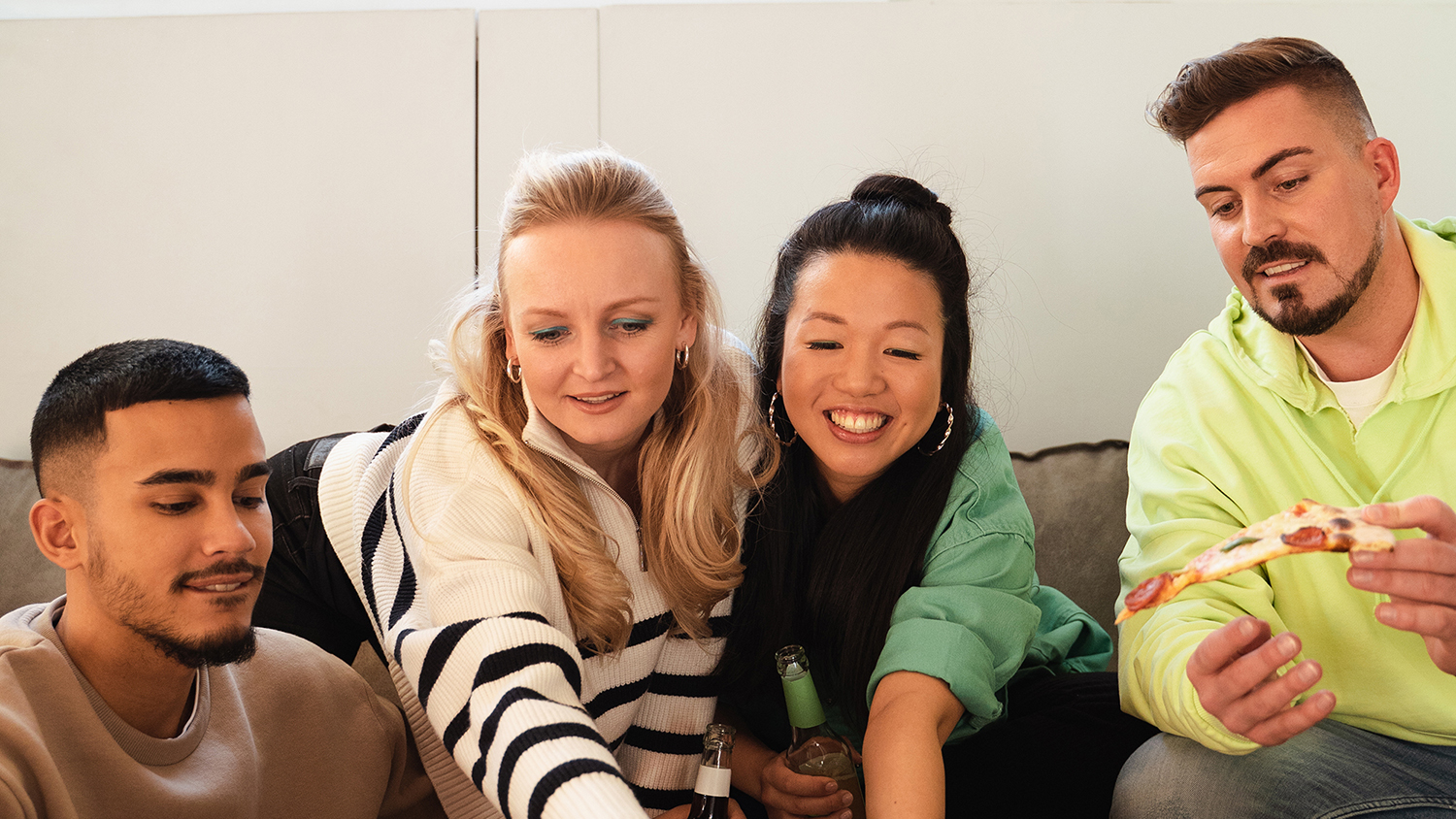 In cosa consiste l’appartamento condiviso? Quattro giovani sorridono seduti insieme su un divano