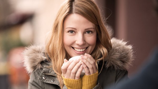 Giovane donna con cappotto si scalda con una tazza – assicurazione infortuni e protezione contro i furti nella stagione fredda.